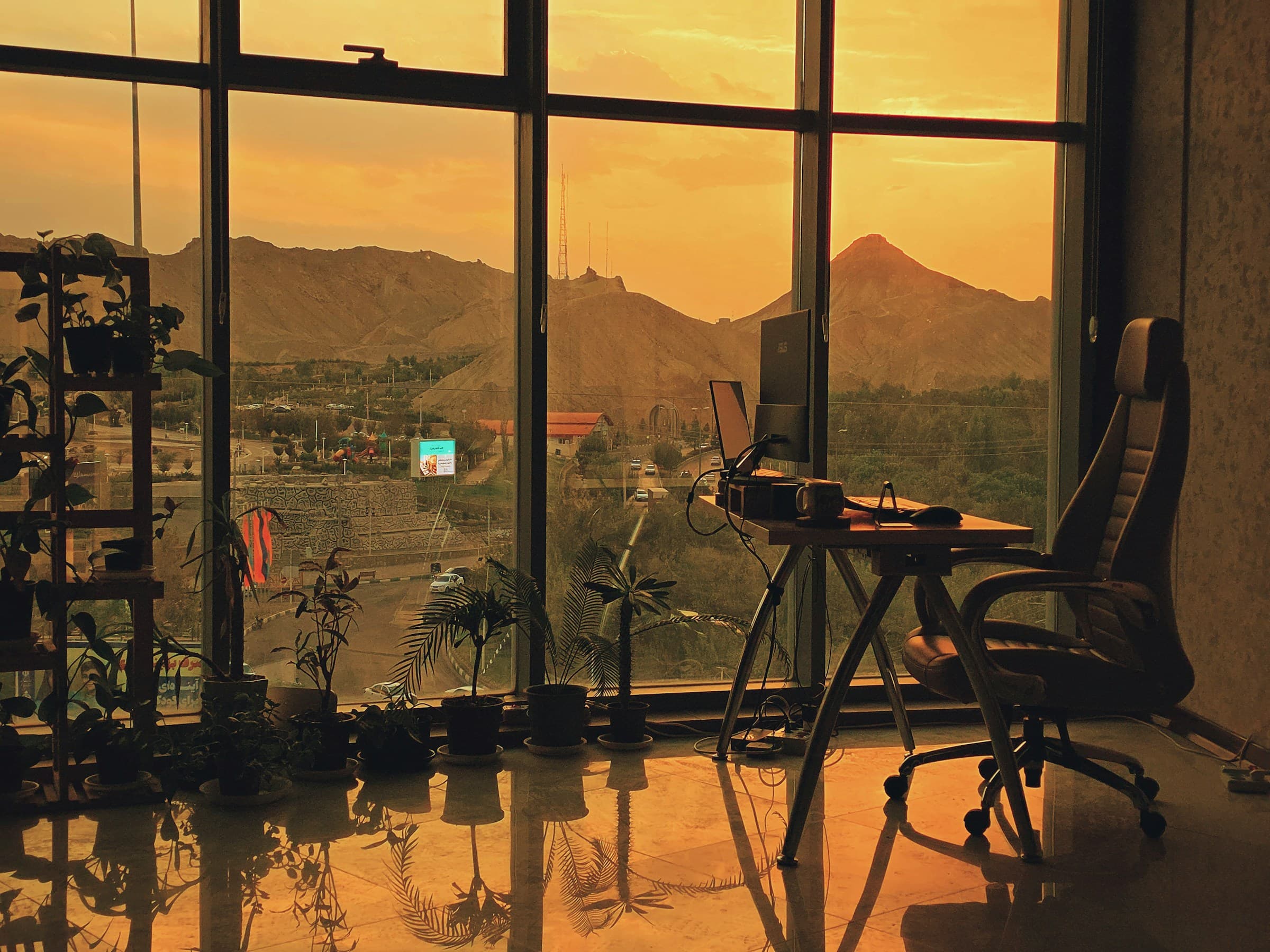 Studio vitré au coucher du soleil : plantes en pot, bureau avec écran et lumière ambrée